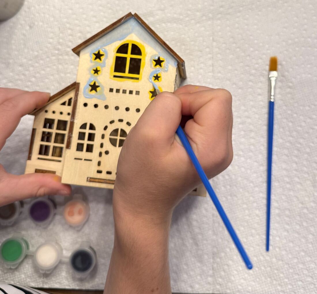 A child painting stars onto the balsa house with a fine brush.